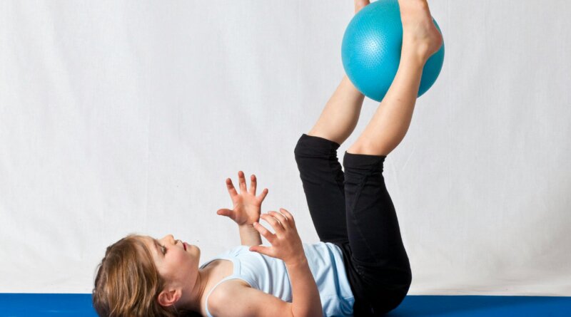 Children, adults, and seniors practicing gymnastics exercises together in a group fitness class.